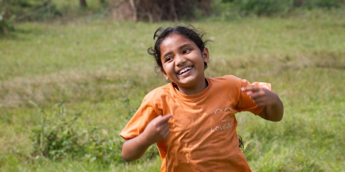 Young girl running and smiling in a grassy field in Nepal